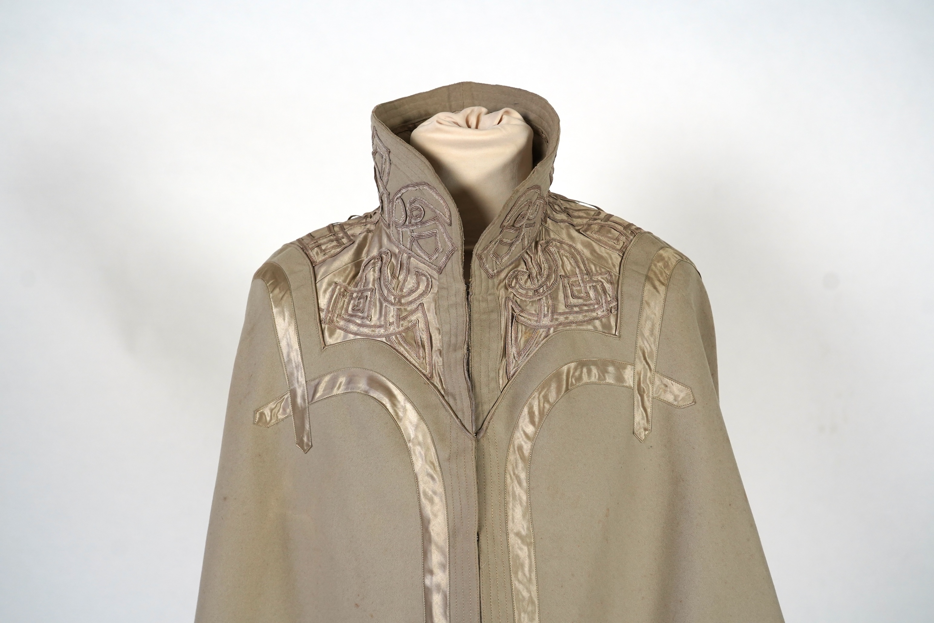 An Edwardian mushroom wool evening cape, decorated with silk ribbon worked strapping and ornate appliquéd fine braiding across the shoulders and under section of the collar, lined with cream silk satin.